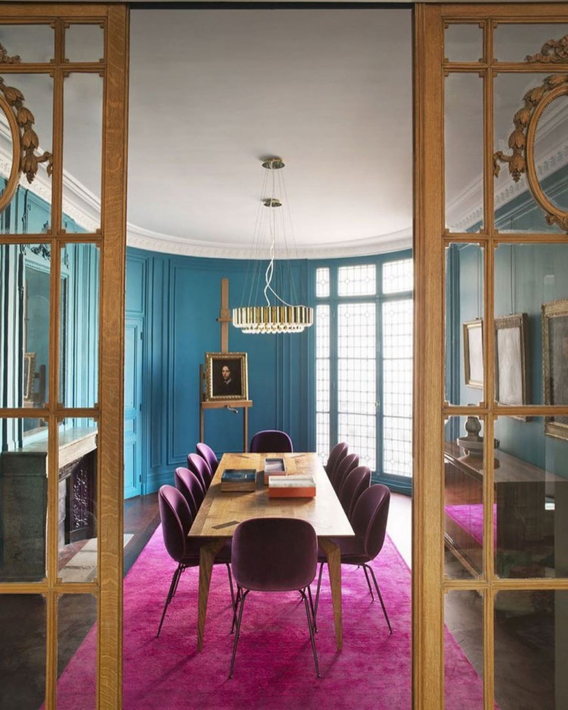 яркая столовая с бирюзовыми стенами, ковром цвета фуксии, с камином, деревянным столом и бархатными стульями винного цвета.jpg