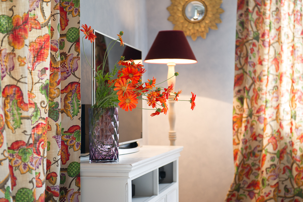 гостиная с белой тумбой под ТВ, торшером, зеркалом-цветком в золотой раме и ярким текстилем в теплых цветах.jpg
