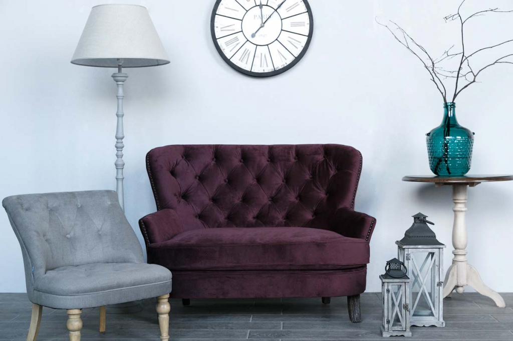 гостиная с бархатным диваном винного цвета, серым бархатным креслом и большими крупными часами над диваном